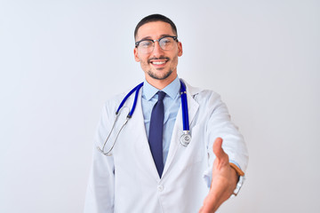 Young doctor man wearing stethoscope over isolated background smiling friendly offering handshake as greeting and welcoming. Successful business.