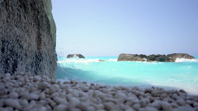 4K closeup of sea waves of turquoise water crashing on a rocky coast and rocks on a bright sunny day, beach vacation in Lefkada, Greece
