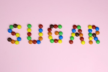 The word Sugar from colored candies on a pink background