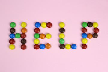 Word help of multicolored candies on pink background