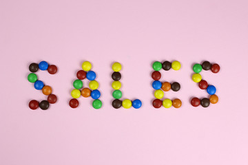 The inscription Sale consists of colored candies on a pink background