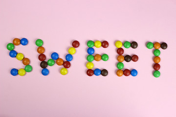 The word sweet are contained by colored candies on a pink background