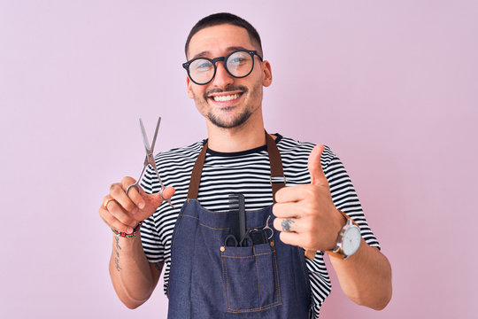Young handsome hairdresser man wearing apron over pink isolated background happy with big smile doing ok sign, thumb up with fingers, excellent sign