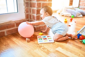 Fototapeta premium Adorable toddler crawling around lots of toys at kindergarten
