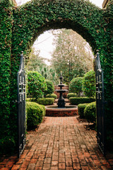Outdoor Green secret garden with arched entry and gate and a fountain in the middle and red brick...