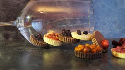 chocolate candies decorated with berries in a glass goblet on a black background