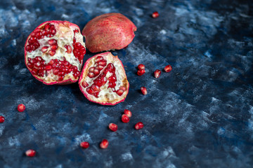 Large pomegranate broken into pieces. On a blue background under a stone. Trend 2020. Grains are scattered nearby.