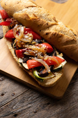 Vegan sub sandwich with grilled vegetables on wooden background