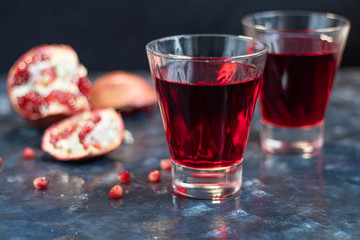 Pomegranate juice in transparent glasses. In the background are parts of a large pomegranate. On a blue background under a stone. Grains are scattered nearby. Trend 2020.