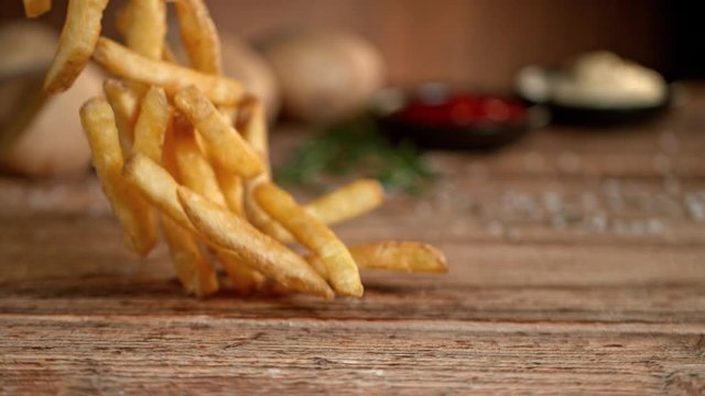 Super Slow Motion Shot of Falling Fresh French Fries on Wooden Table and Adding Salt at 1000fps.