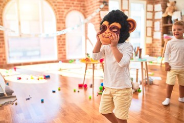 Adorable blonde twins playing wearing monkey mask around lots of toys at kindergarten