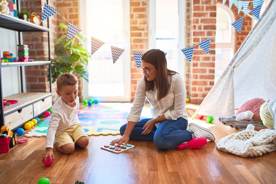 Beautiful teacher and toddler learning maths using numbers puzzle game around lots of toys at kindergarten