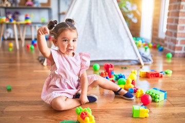 Young beautiful toddler sitting on the floor playing with building blocks at kindergaten