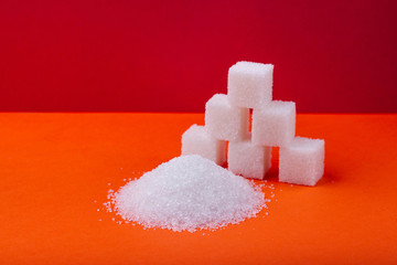 Cubes of white sugar and granulated sugar on an orange background