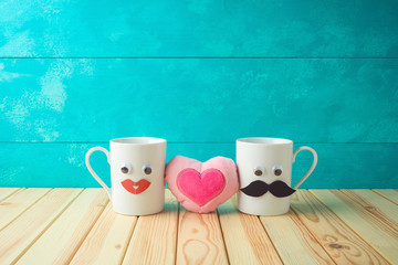 Valentines day concept with coffee cup funny characters and heart shape on wooden table over blue background.