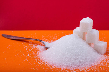 Spoon and cubes of white sugar and granulated sugar on an orange background
