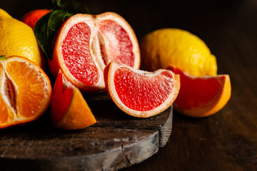 Obraz na płótnie Canvas Slices of ripe fresh organic citrus fruits: grapefruit, orange, lemon on wooden board. Natural source of vitamins, low calories tasty dessert. Dark background, close up, front view