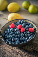 bowl of fresh blueberries and raspberries on wooden table with other fruits