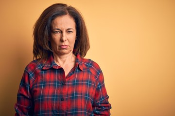 Middle age beautiful woman wearing casual shirt standing over isolated yellow background skeptic...
