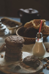 oat cookies with chocolate and milk in a designes vintage lamp bottles on a wooden table with nuts and spices