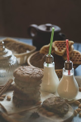 oat cookies with chocolate and milk in a designes vintage lamp bottles on a wooden table with nuts and spices
