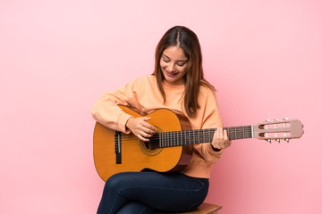 Fototapeta premium Young brunette girl with guitar over isolated pink background