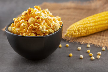 Popcorn in the black bowl and raw corn on the black table. High angle view.