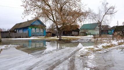 Puddles instead of snow. A Country road in the village, flooded with water. A giant puddle of melted snow. Village house. Abnormal warming in Russia. 