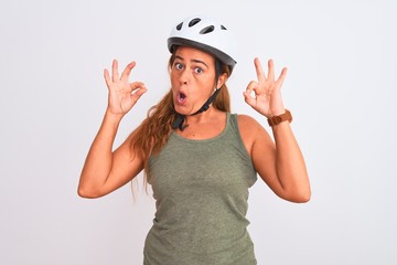 Middle age mature cyclist woman wearing safety helmet over isolated background looking surprised and shocked doing ok approval symbol with fingers. Crazy expression
