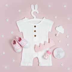 Set of baby clothes and accessories for little Princess on pink background. White bodysuit on cute hanger with bunny ears and shoes, cotton crown and toys. Fashion newborn. Flat lay, top view