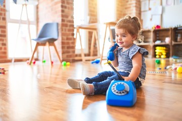 Beautiful toddler sitting on the floor playing with vintage phone at kindergarten