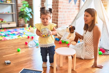 Young beautiful teacher playing with dog doll and toddler holding jar of chocolate balls at...