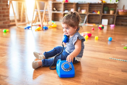 Beautiful toddler sitting on the floor playing with vintage phone at kindergarten