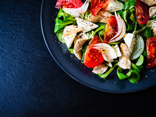 Caesar salad -  barbecue chicken breast, vegetables and feta cheese on black stone background