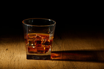 Whiskey with ice or brandy in a glass and a square carafe on an old wooden background. Whiskey with...