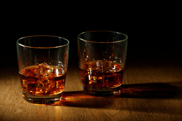 Whiskey with ice or brandy in a glass and a square carafe on an old wooden background. Whiskey with ice in a glass. Whiskey or cognac. Selective focus.