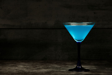 Blue cocktail in a glass for martini on a gray background. Blue cocktail with martini on a gray stone background.