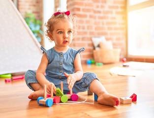 Beautiful caucasian infant playing with toys at colorful playroom. Happy and playful with wooden train pieces at kindergarten.