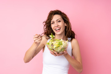 Young woman with curly hair holding a salad over isolated pink background