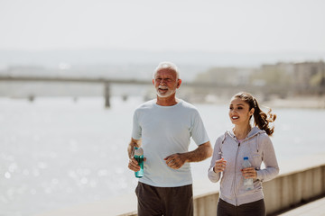 Fit senior man in good shape jogging and exercising together with his young adult daughter coach or...