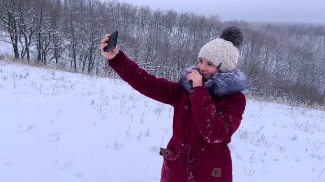 teenager young caucasian girl taking selfie photos on smartphone and posing for a photo in the Russian winter snowy forest. Healthy open air spending holidays or weekend outdoors in cold weather.