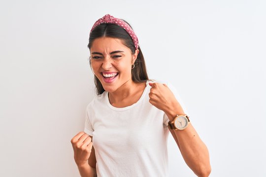 Young beautiful woman wearing casual t-shirt and diadem over isolated white background very happy and excited doing winner gesture with arms raised, smiling and screaming for success. Celebration
