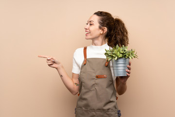 Gardener woman holding a plant pointing to the side to present a product