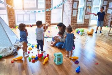 Beautiful teacher and group of toddlers playing around lots of toys at kindergarten