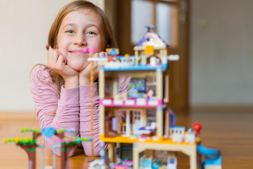 Little girl plays with a children's constructor at home. Little girl playing with lots of colorful plastic blocks constructor and builds house