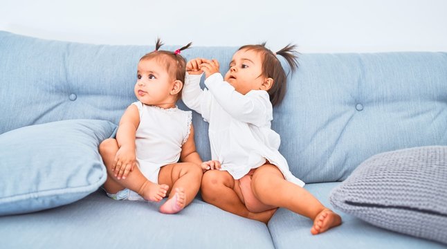 Beautiful infant happy girls playing together at home kindergarten sitting on the sofa