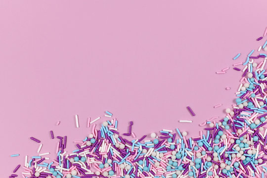 Colorful white, pink, blue and purple sugar sprinkles in shape of balls and sticks on pink background with blank copy space