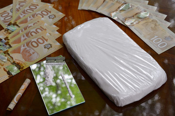 Large bag of cocaine and coke line with razor blade on mirror on table with Canadian money