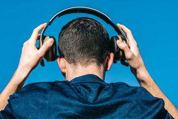 caucasian Young guy from back putting on music headphones on blue background