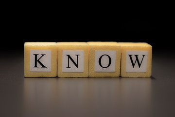 The word KNOW written on wooden cubes isolated on a black background...